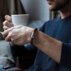 Man holding coffee cup and wearing leather bracelet with engraved magnetic clasp silver by Fischers Fritze