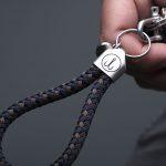 Hand holds keychain sailing rope navy blue brown, stainless steel frame with engraving visible